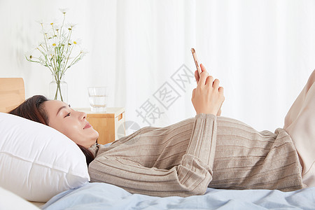 孕妇在床上开心的玩手机图片