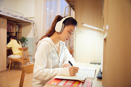 夜晚女学生戴着耳机在宿舍认真复习功课高清图片