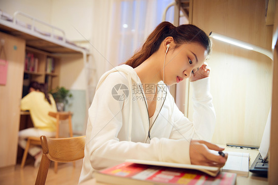 夜晚女学生戴着耳机在宿舍认真复习功课图片