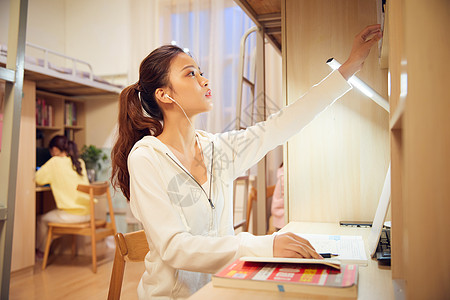 夜晚女学生戴着耳机在宿舍认真复习功课图片