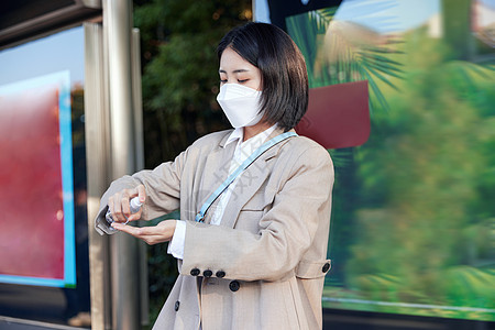 戴口罩在公交站台等待公交车的女性手部消毒图片