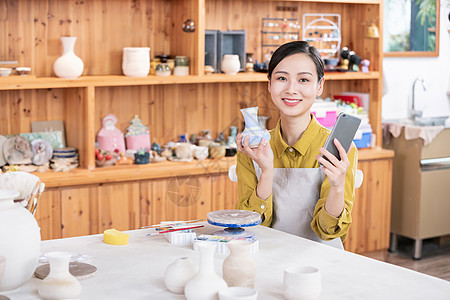 美女拿手机拍摄陶艺半成品背景图片