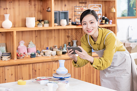 美女拿手机拍摄陶艺半成品背景图片