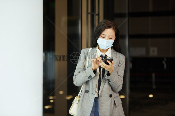 戴口罩的女白领下班低头玩手机图片