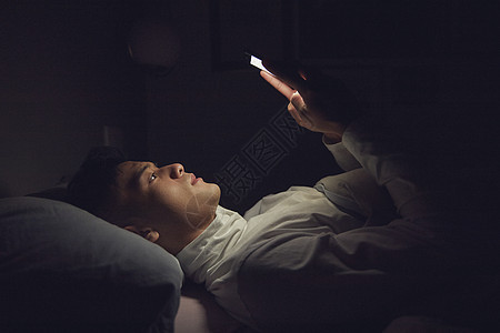 年轻男士深夜躺在床上玩手机图片