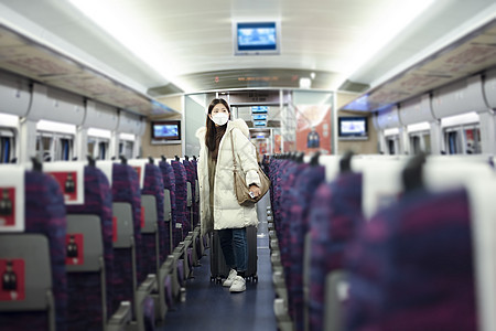 戴口罩的女性拉着行李箱在火车车厢里寻找座位图片