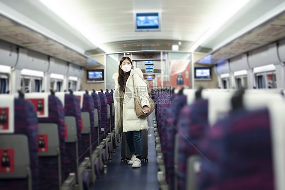 戴口罩的女性拉着行李箱在火车车厢里寻找座位图片