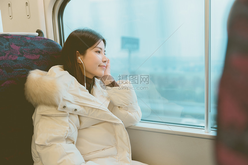 坐在火车上戴着耳机看窗外风景的女性图片