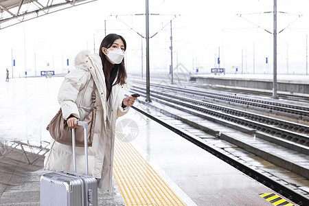 拉着行李箱戴口罩在站台等车的女性图片