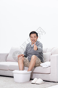 老年男性坐在沙发上使用泡脚盆点赞图片