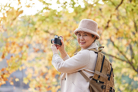 老人逛公园拿相机拍摄秋季风景图片