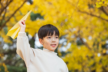 秋季小男孩银杏树下扔纸飞机图片