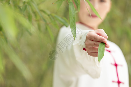 穿着练功服的女性单手夹着一片竹叶特写图片