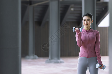 运动衣女性在户外用哑铃健身背景