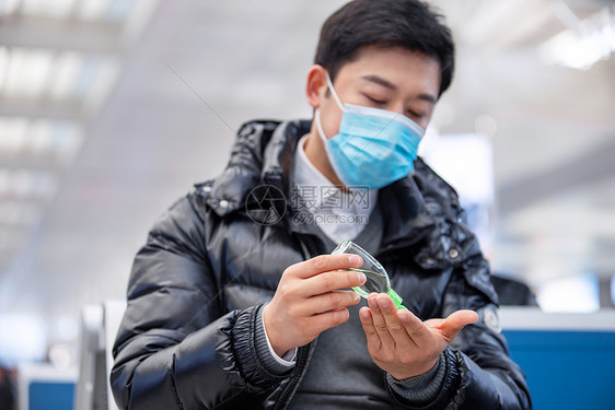 疫情期间戴着口罩候车的男性使用酒精消毒液图片