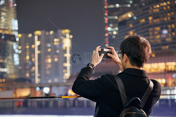 男青年用手机拍摄城市夜景图片