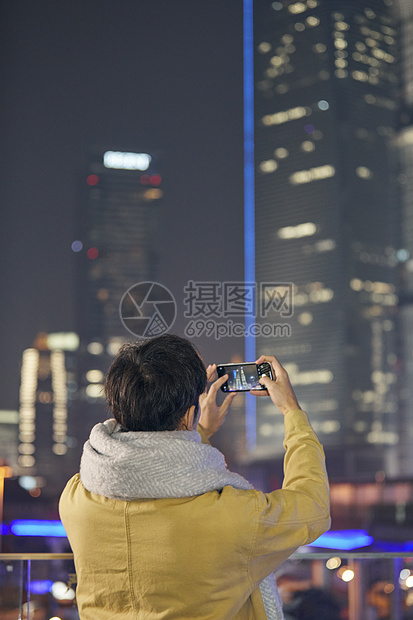 夜晚男青年用手机拍摄城市夜景图片
