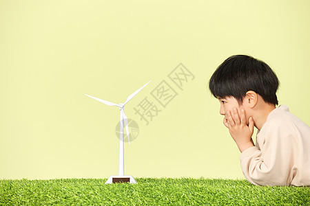 趴在草地上看着风力发电机模型的小男孩图片
