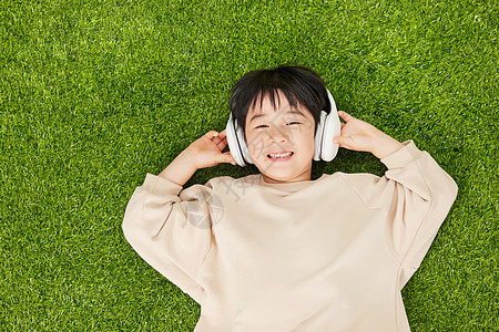 戴着耳机躺在草坪上的小男孩双手抓耳机图片