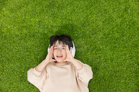 戴着耳机躺在草坪上的小男孩做呐喊动作图片
