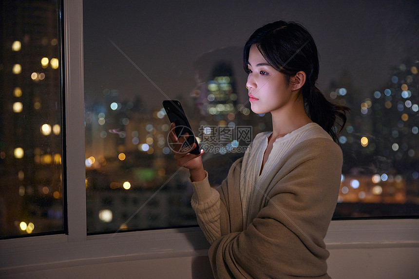 深夜阳台玩手机的年轻女性图片