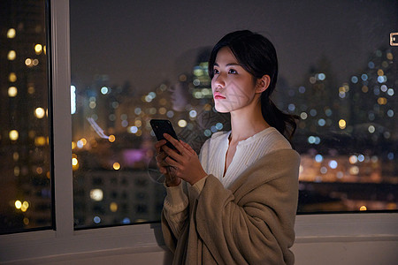 深夜阳台玩手机的年轻女性图片