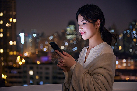 夜晚阳台深夜阳台玩手机的年轻女性背景