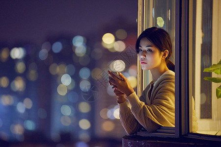 阳台夜景深夜阳台玩手机的年轻女性背景