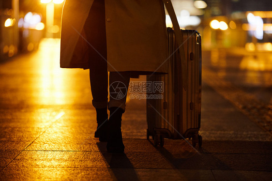 夜晚都市女性手提行李箱走在路上图片