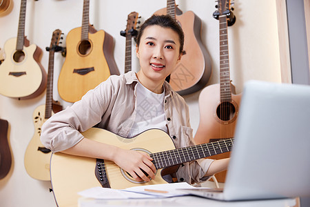 面对电脑线上学习吉他的女性图片