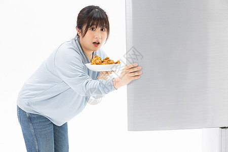 肥胖女性从冰箱里拿出一盘食物图片