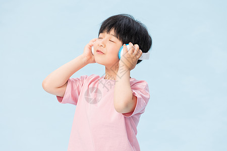 小学生手捂耳朵童真小男孩戴耳机听音乐背景