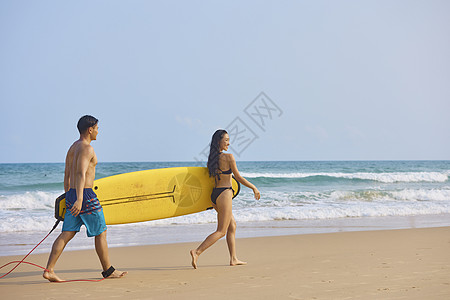 情侣性感写真年轻男女手拿冲浪板海边行走背景