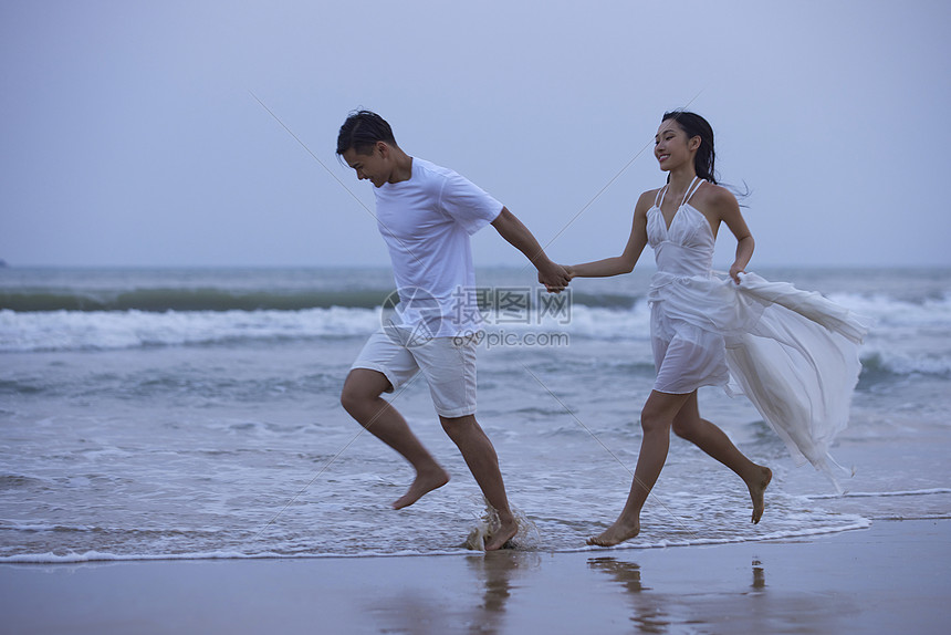 傍晚年轻情侣海边牵手奔跑图片