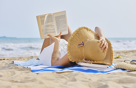 年轻美女度假躺在沙滩看书图片