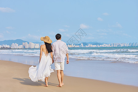 沙滩度假美女年轻情侣牵手海边散步背影背景