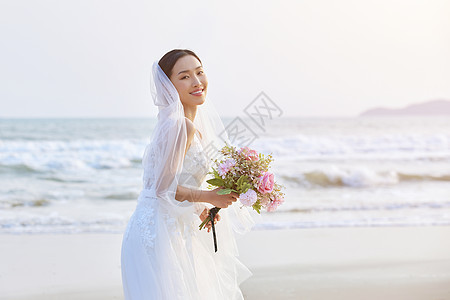 海边穿婚纱的美女手拿手捧花背景图片