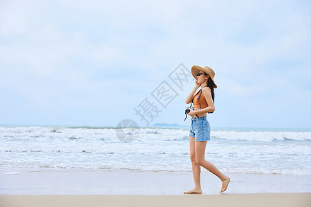 年轻美女手拿相机海边旅行图片