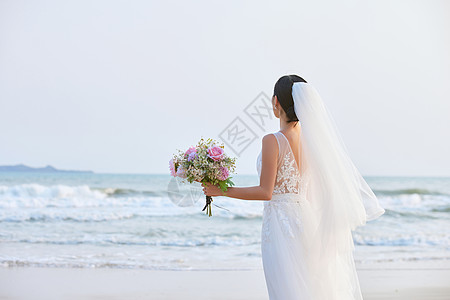 海边穿搭海边穿婚纱的美女手拿手捧花背影背景