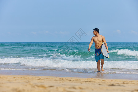 年轻男士拿着冲浪板海边行走图片