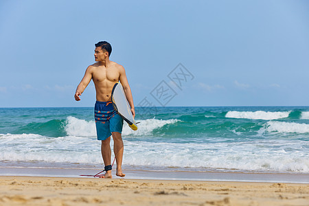 海边日落年轻男士拿着冲浪板海边行走背景