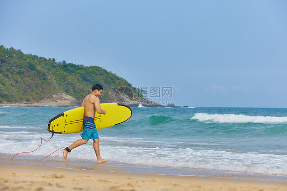 男青年抱着冲浪板奔向大海图片