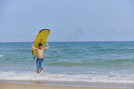 年轻男士举着冲浪板走向岸边图片