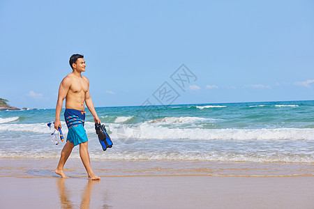 男青年拿着潜水装备在海边行走图片