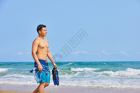 男青年拿着潜水装备在海边行走图片
