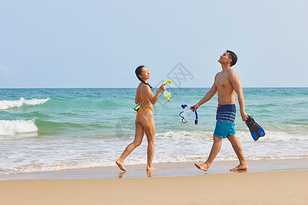 年轻情侣拿着潜水装备海边行走图片