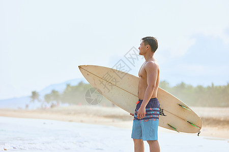 年轻男士拿着冲浪板海边行走背景图片