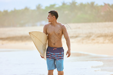 年轻男士拿着冲浪板海边行走背景图片