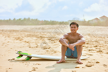 年轻男士坐沙滩上拿着冲浪板图片