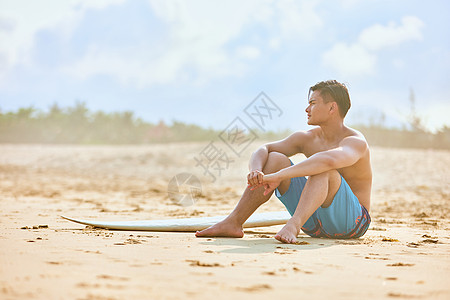 年轻男士坐沙滩上拿着冲浪板图片